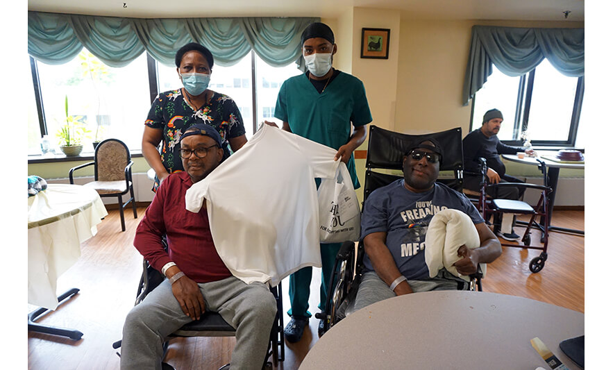 Extended Care Adopt-a-Resident Day 5-11-2022 Men get hats and shirts from two employees for web